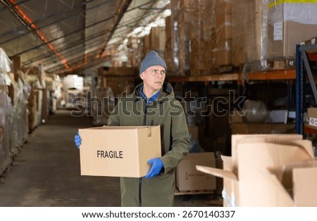 Storekeeper man stacking pasteboard box in storehouse during working day.