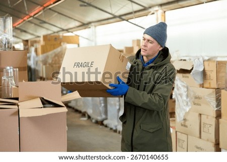 Storekeeper man stacking pasteboard box in storehouse during working day.