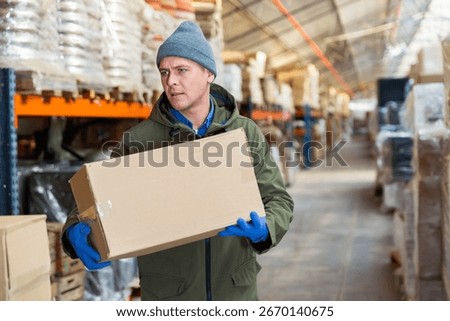 Storekeeper man stacking pasteboard box in storehouse during working day.