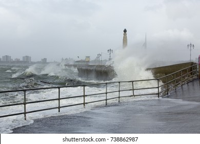 Storm Brian Comes To Southsea. View Looking Along The Southsea Beaches Towards Old Portsmouth. Naval War Memorial And Spinnaker Tower In The Background. The Sea Making The Coastal Path Treacherous.