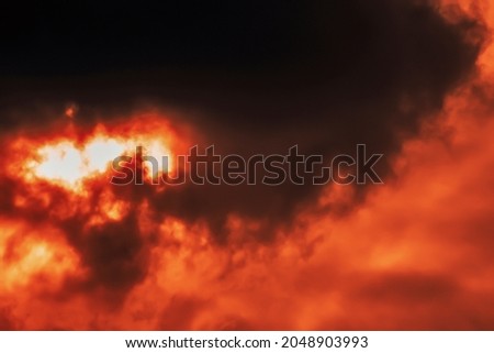 Storm cloud loomed and obscured the disk of the luminary, which is barely visible, in intense reddish rays of the sunset, creating a dramatic setting. Red haze. Selective focus.