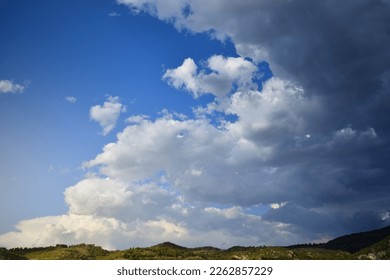 Storm clouds advance on a clear blue sky over a narrow mountainous horizon - Powered by Shutterstock