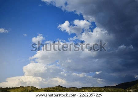 Storm clouds advance on a clear blue sky over a narrow mountainous horizon