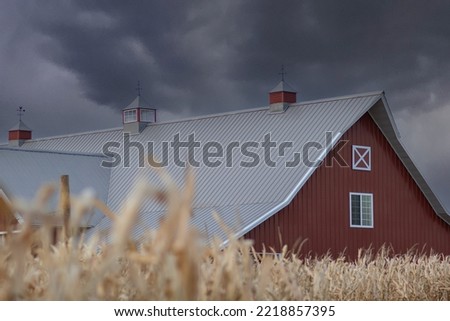 Storm clouds gather over a red barn in a corn field in the midwest