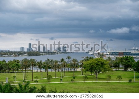 Storm clouds over Biscayne Bay and Port of Miami. Wide view of Miami bay with green park in foreground and cruise ships at the port under dramatic dark storm clouds.