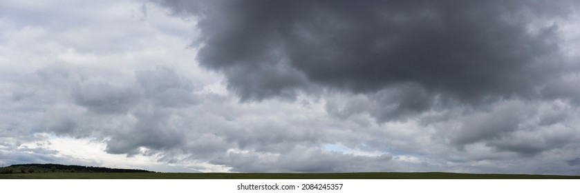 Storm clouds over the fields. Landscape at sunset. Tragic gloomy sky. Panorama. The sun is hidden.