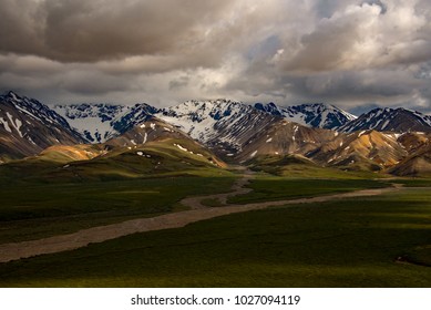 Storm clouds over Polychrome Pass - featuring snow-capped mountains and a braided river - in Denali National Park, Alaska