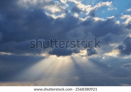 Storm cloudscape with sunbeams on a dramatic sky. Sun rays shining through the dark rainy clouds. Nature composition. 