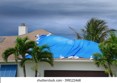 Storm damaged roof on house with a protective blue plastic tarp spread over hole in the shingles and rooftop. - Shutterstock ID 398122468
