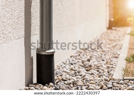 Storm Drainage Drain Downspout Pipe  Installing into French drain with  Drainage Stones Outside Building. Stormwater pipe on facade with Drain Gravel 