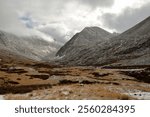 A storm front over a narrow valley covered with the first snow at the junction of two rocky mountain peaks. Sailyugemsky Ridge, Altai, Siberia, Russia.