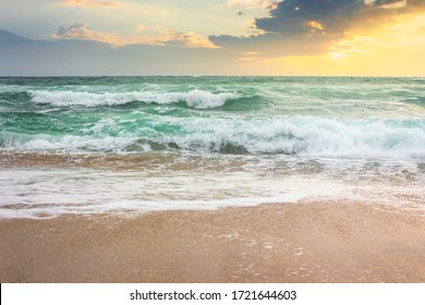 Storm On The Sandy Beach At Sunrise. Dramatic Ocean Scenery With Cloudy Sky. Rough Water And Crashing Waves In Morning Light