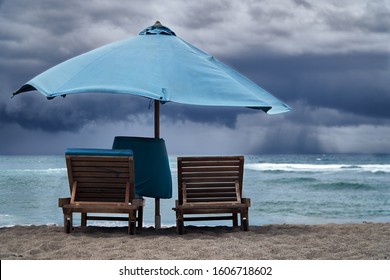 Storm On The Sea With Thunderclouds. Empty Beach With Umbrella And Sun Beds On Background Of Hard Rain Over Ocean.