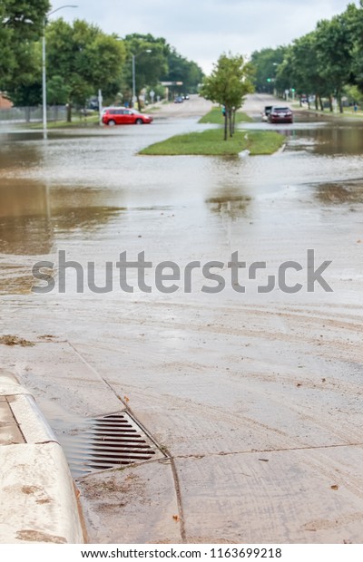 Storm water filling a flooded sewer drain\
to the top with stalled cars in the\
background