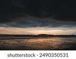 Storms clouds with Rays of sunlight and dark ocean in Thailand. Powerful dramatic storm cell over ocean beach. Dramatic view of waves washing ashore under a dark storm clouds on a tropical beach.