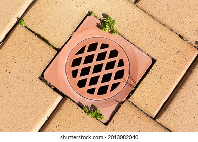 A Stormwater Drain Cover Inserted In Brown Paving Stones Near A Swimming Pool