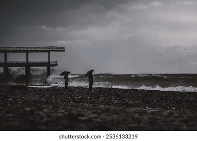 Stormy beach scene with people and umbrellas
 Two people with umbrellas stand on a rocky shore, facing crashing waves and dark clouds in a dramatic, stormy seaside setting.
 - Powered by Shutterstock