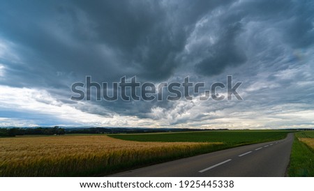 Stormy clouds, dramatic sky above rural farmland and asphalt road