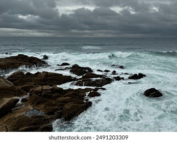 Stormy Coastal Waves Crashing Against Rocky Shoreline with Overcast Sky and Dark Clouds. - Powered by Shutterstock