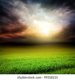 Stormy Dramatic Sky And Green Field Of Grass With Sun Light Passing Through The Clouds In The Evening