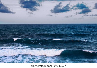 A Stormy Ocean A Dusk With Large Waves And Two Surfers In The Distance