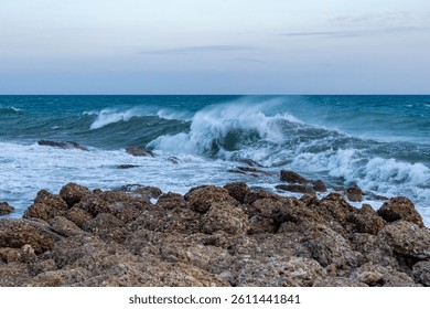 Stormy sea waves crashing against rocky shore during cloudy evening. Side, Turkey, Mediterranean coast.