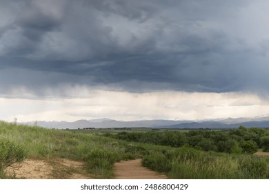 A Stormy Sky Over Green Grassy Fields and Snow-Capped Mountains in Colorado - Powered by Shutterstock