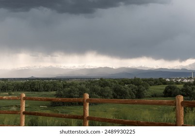 A Stormy Sky Over Green Rolling Hills and Snow Capped Mountains in Colorado - Powered by Shutterstock