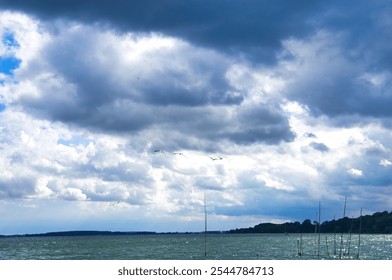 Stormy sky over a lake. Dark clouds contrast with rays of sunlight that make the water sparkle. Four birds fly in the foreground.