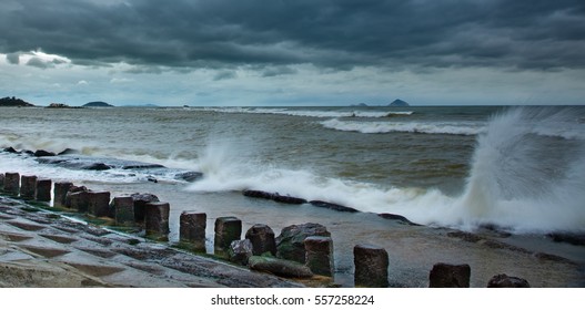 Stormy Weather And A Concrete Structure Coastline Barrier With The Ocean Beyond And Islands In The Background.