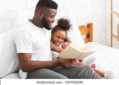 Story Time. Loving African American Dad Reading Fairy Tales To His Little Daughter, Sitting Together On Bed