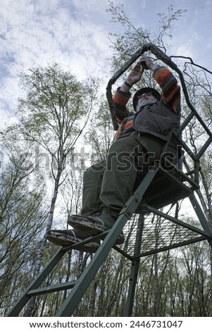 A stout man sits into a hunter's high stand in a beautiful bog area and takes photos