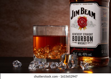 St.Petersburg, Russia - December 2019 - Bottle of Jim Beam bourbon whiskey and glass with drink and ice  on wooden table on brown background. Kentucky straight bourbon whiskey