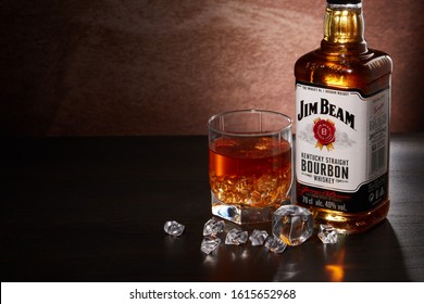 St.Petersburg, Russia - December 2019 - Bottle of Jim Beam bourbon whiskey and glass with drink and ice  on wooden table on brown background with copy space. Kentucky straight bourbon whiskey