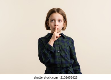 Strabismus Kid Little Girl 9s Wearing Plaid Shirt Dress Making Silence Gesture With Finger On His Lips. Child Have A Crossed Eye. Health Problem. Healthcare And Medicine Concept