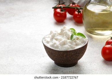 Stracciatella cheese on grey background with oil, basil and tomatoes. Italian Stretched curd cheese product Stracciatella in bowl. Copy space