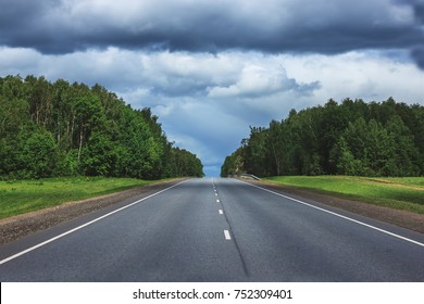 Straight  Asphalt Country Road. Open Road Through Spring Fields And Meadows In Sunny Evening. Landscape At The Sunny Day And Beautiful Cloudy Sky In Overcast
