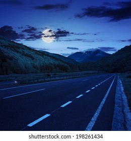 Straight Asphalt Road In Mountains Passes Through The Green Shaded Forest At Night In Moon Light Composite