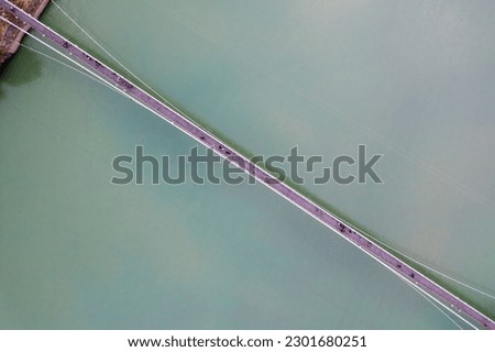 straight down decending aerial drone shot of ram setu suspension bridge over the fast flowing blue waters of ganga in the holy city of rishikesh India
