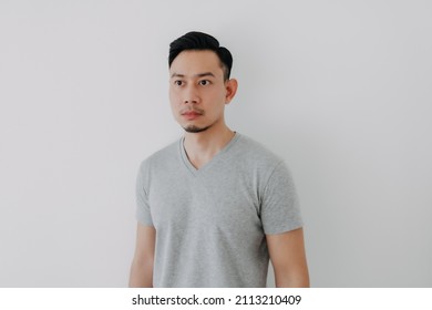 Straight Face Portrait Of Serious Asian Man In Grey T-shirt On White Wall.