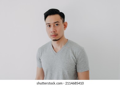 Straight Face Portrait Of Serious Asian Man In Grey T-shirt On White Wall.