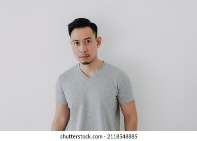 Straight Face Portrait Of Serious Asian Man In Grey T-shirt On White Wall.