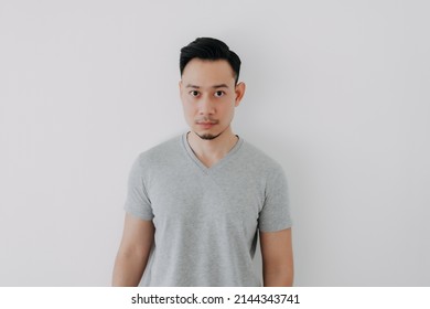 Straight Face Portrait Of Serious Asian Man In Grey T-shirt On White Wall.