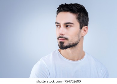 Straight Glance. Handsome Calm Young Man Being Pleased And Cheerful While Standing Against The Blue Background And Looking Left