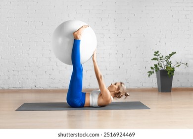 Straight leg hip crunch exercise with props. Fit Caucasian woman does workout with fitness ball in loft studio indoor. Training, balance, pilates, health, gymnastics, concept. - Powered by Shutterstock