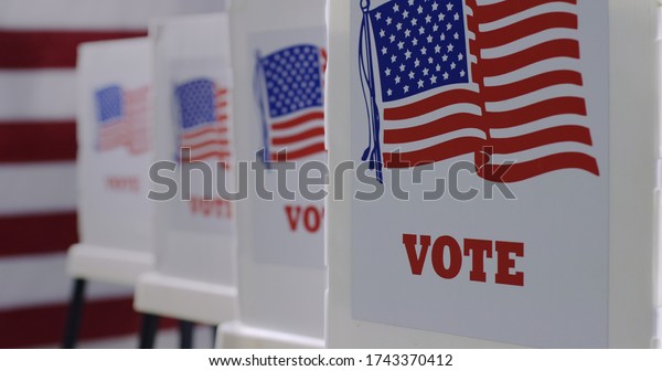 Straight on row of\
voting booths at polling station during American election. US flag\
in background.