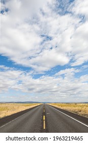 A Straight Road Of Blacktop Going To A Vanishing Point In The Open And Flat Country Of Grant County In Eastern Washington State.  The Cloud Layer Above Is Broken With Pockets Of Blue Sky