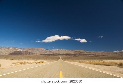 Straight Road In Death Valley Heading Into The Mountains With Wispy Clouds Overhead