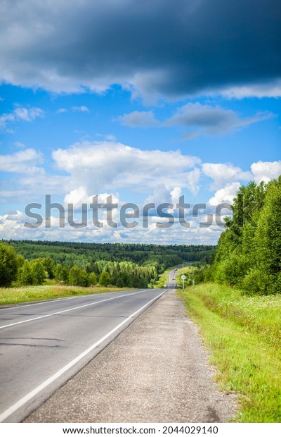 Straight road with a marking on the nature\
background. Open Road in future, no cars, auto on asphalt road\
through green forest, trees. Clouds on blue sky in summer,\
sunshine, sunny day. Bottom\
view