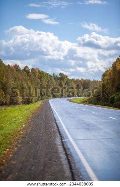 Straight road with a marking on the nature\
background. Open Road in future, no cars, auto on asphalt road\
through green forest, trees. Clouds on blue sky in summer,\
sunshine, sunny day. Bottom\
view